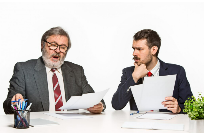 Two businessmen, one looking shocked and the other confused, while reading documents at a desk.