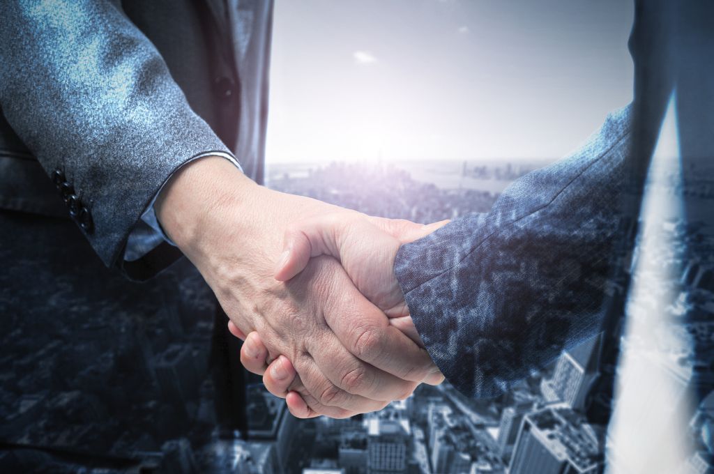 Double-exposure image of two businesspeople shaking hands, overlaid with a city skyline.